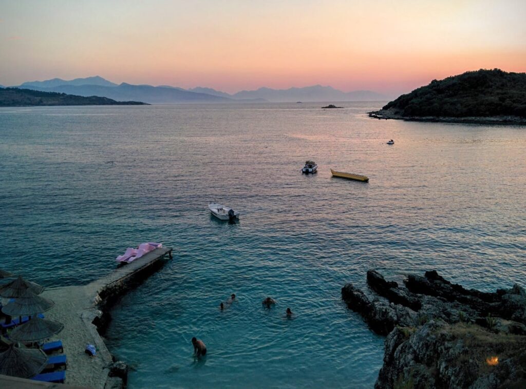 A photo of a beautiful cove in Albania, with beautiful water, and people swimming.