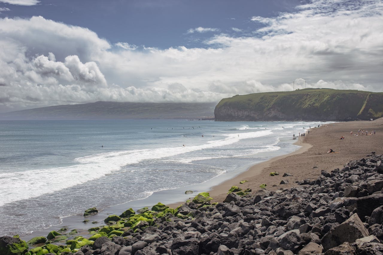 A beach and ocean with surfers surfing and people walking on the sand