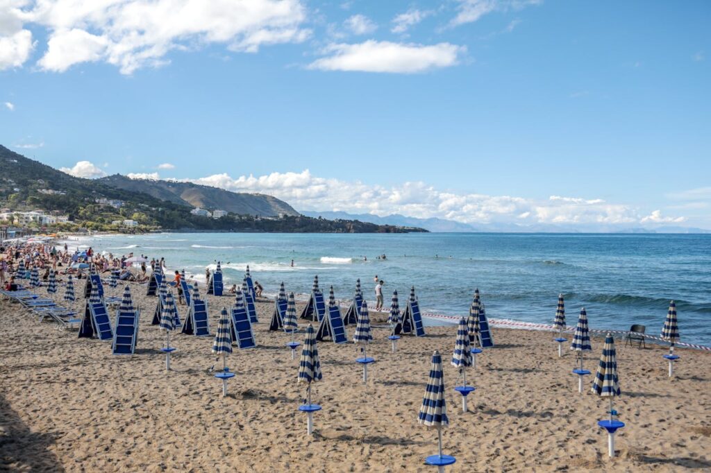 Sicily beach with umbrellas and some people surfing in the background