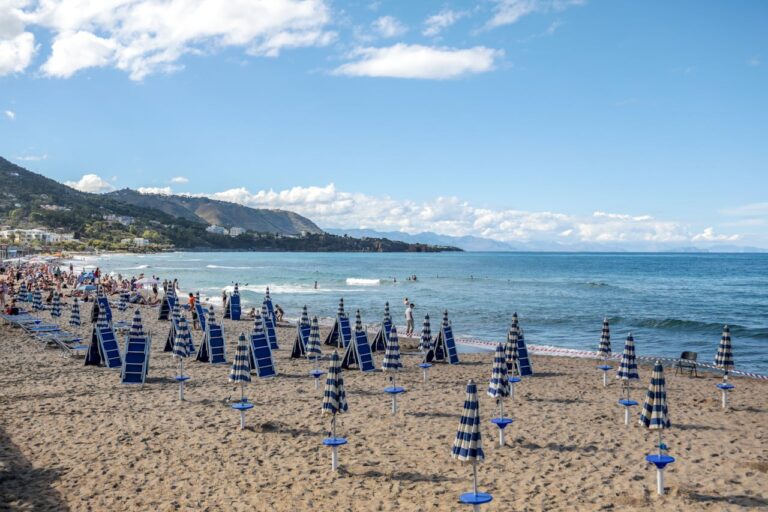 Sicily beach with umbrellas and some people surfing in the background