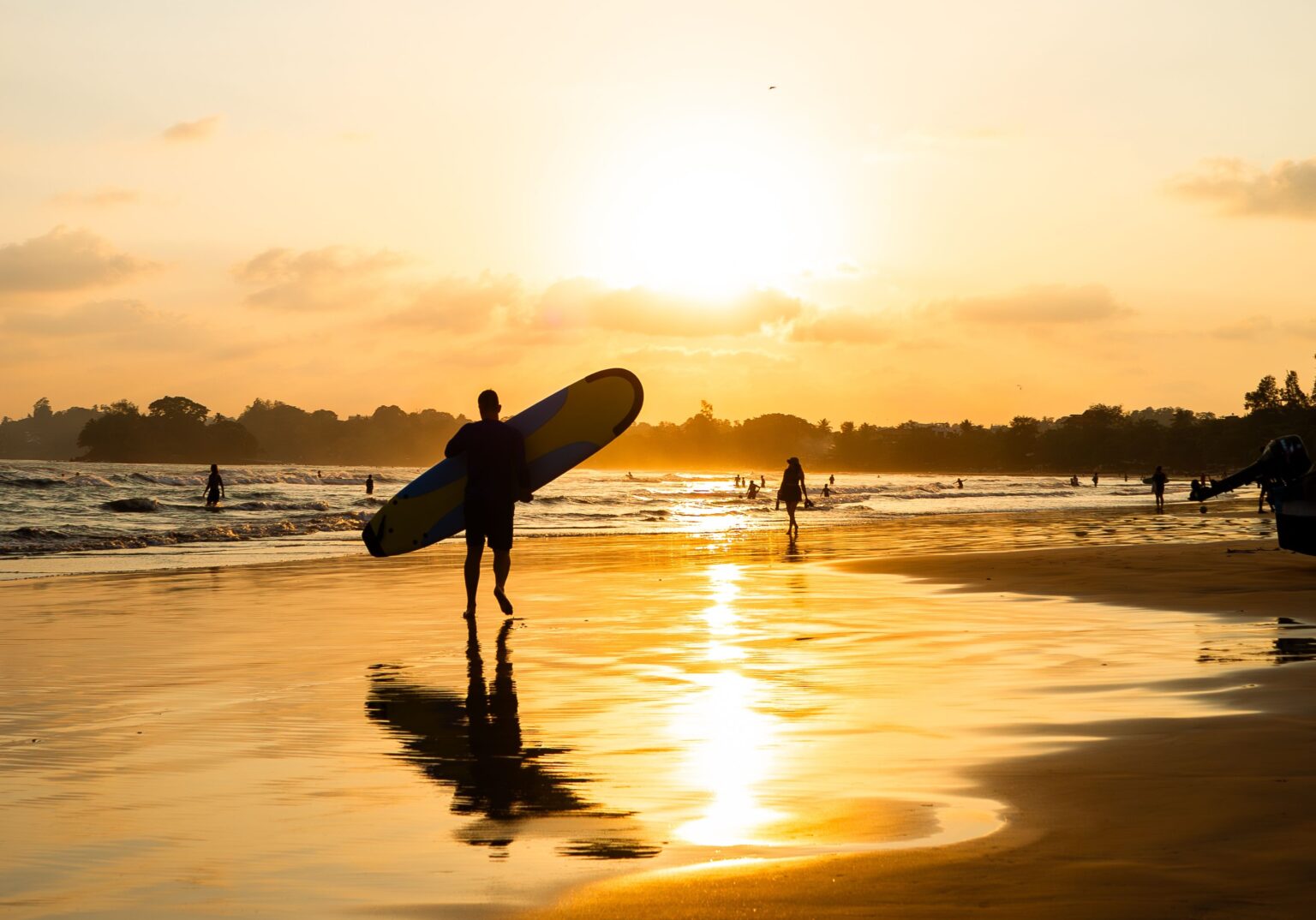 A sunset over the tropical bay of Weligama, with a surfer posing with a longboard.