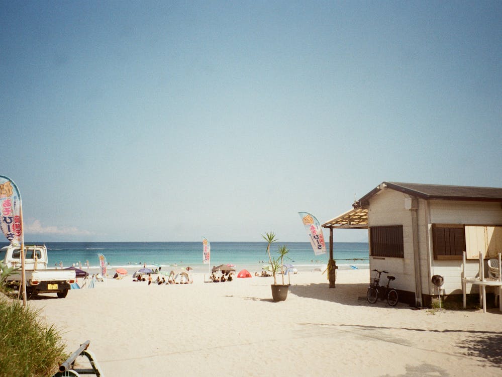 A photo of a beach with sand, buildings, and people sitting on the beach