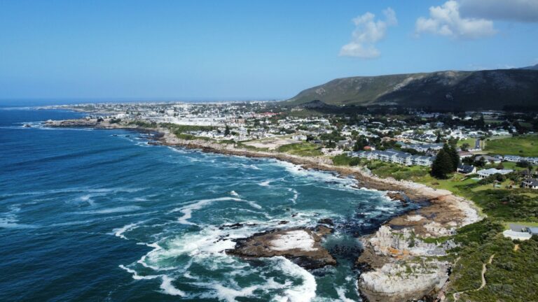 A beautiful drone shot of Hermanus in its full beauty with mountains, the city, waves, and water.
