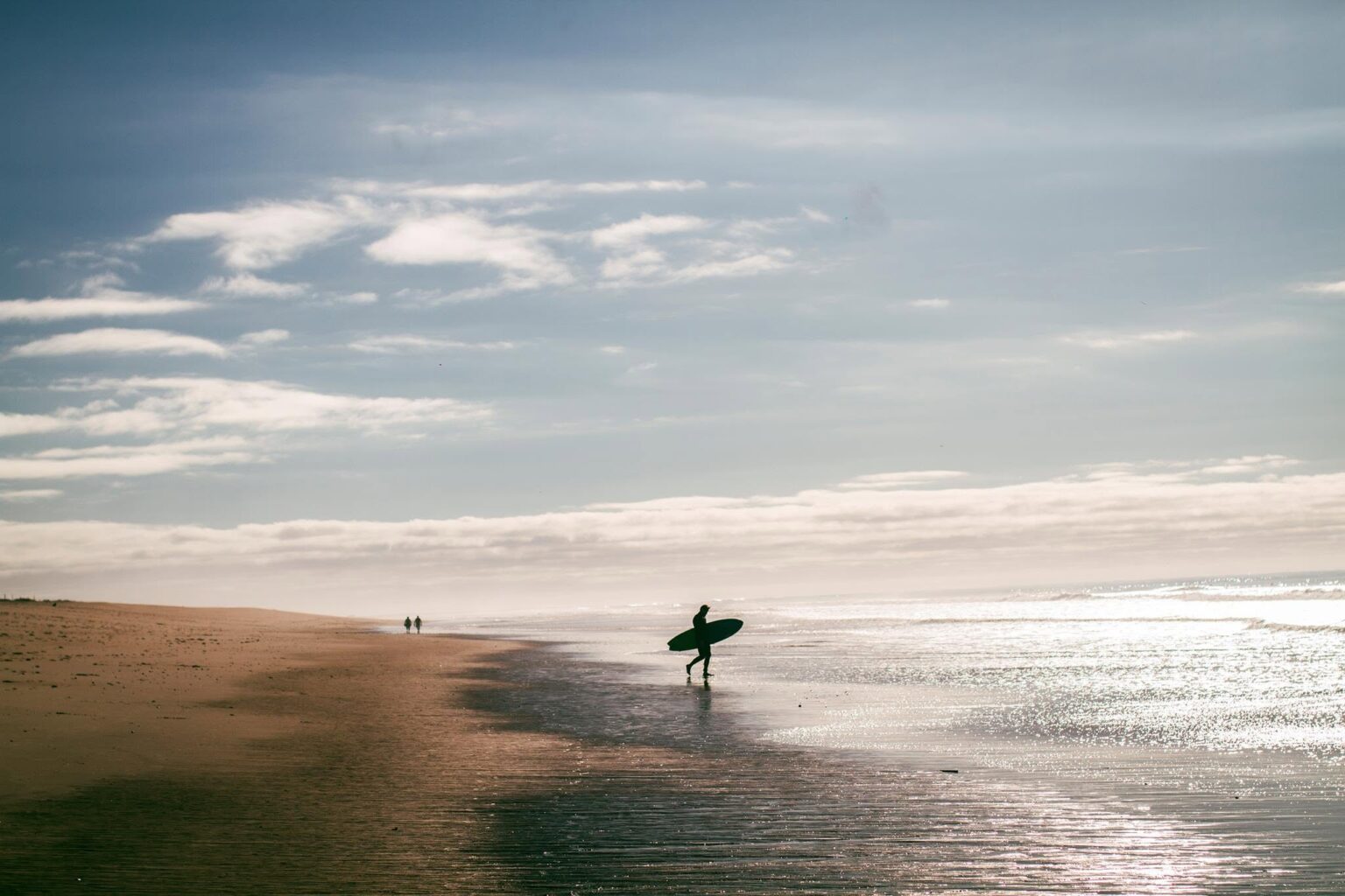 A surfer walking out to the waves on Praia de Faro. Photo provided by AMAR Surfing Academia