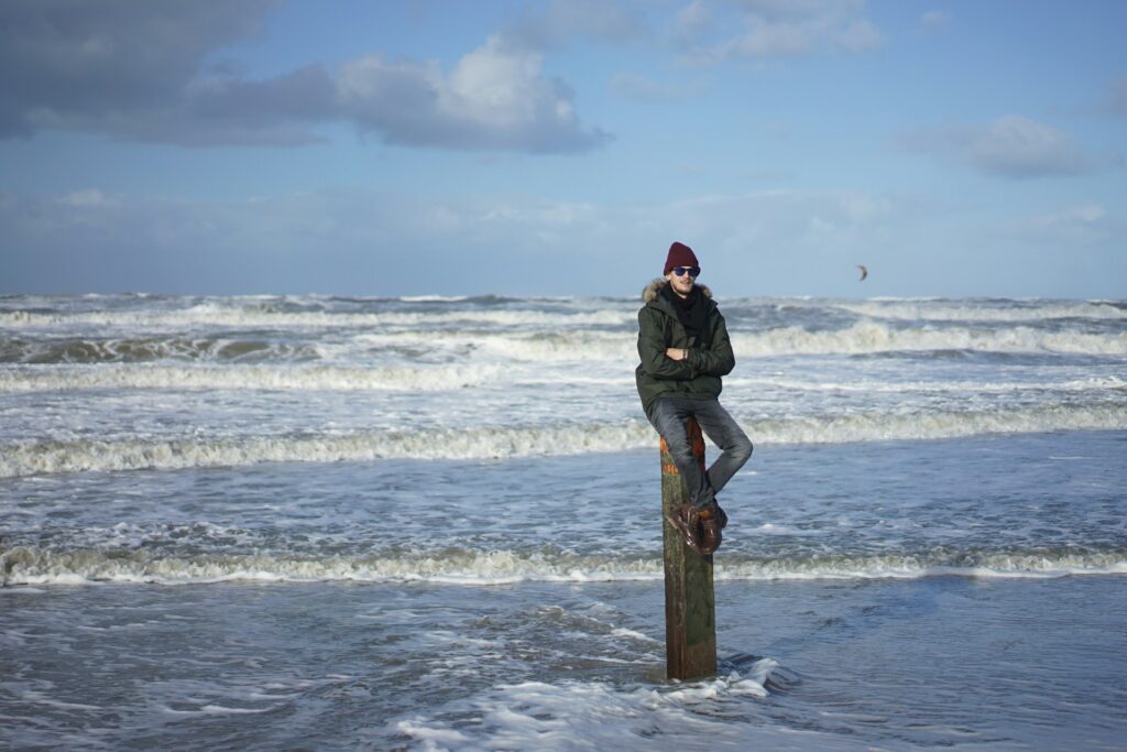 A person sitting on a pilling with waves breaking in the background.