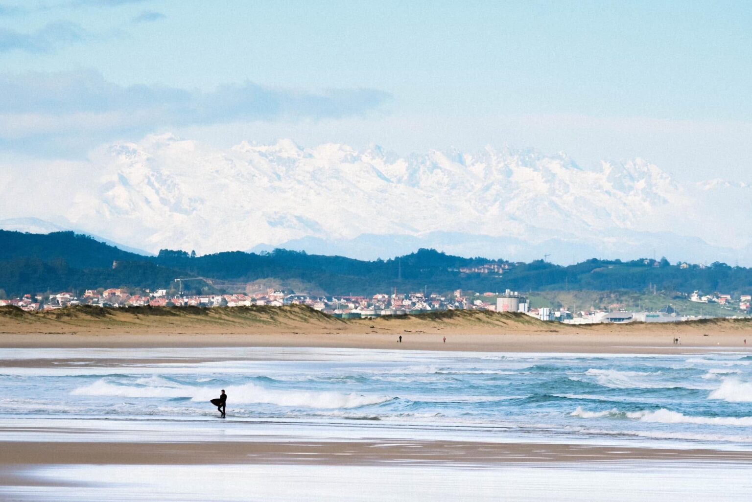 A beautiful shot by Latas Surf of an individual getting out of the water with snow lighten mountains in the background.