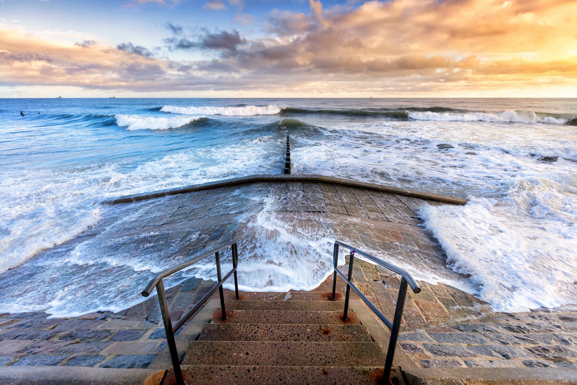 A unique sunset with some surfers riding waves.