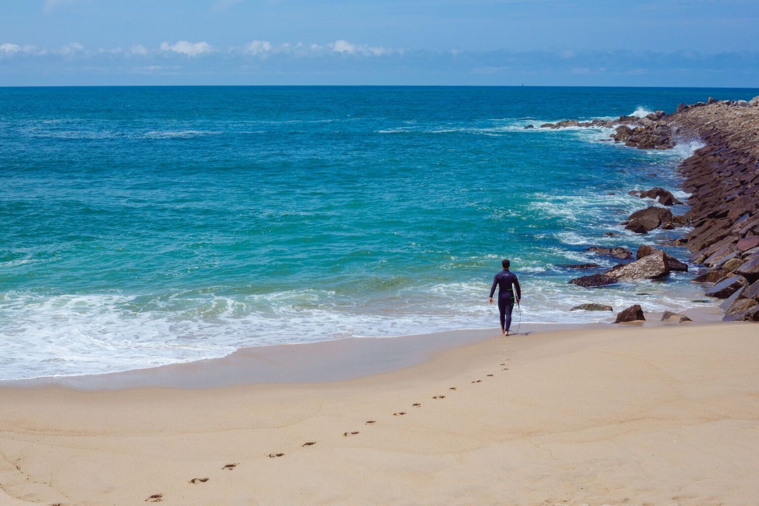 A surfer walking out alongside one of the rock jetties in Espinho.