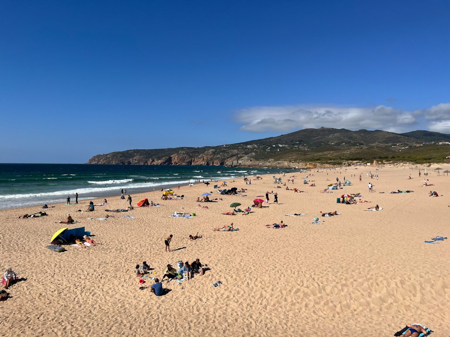 A landscape view of Praia do Guincho with people splayed out over the sand.