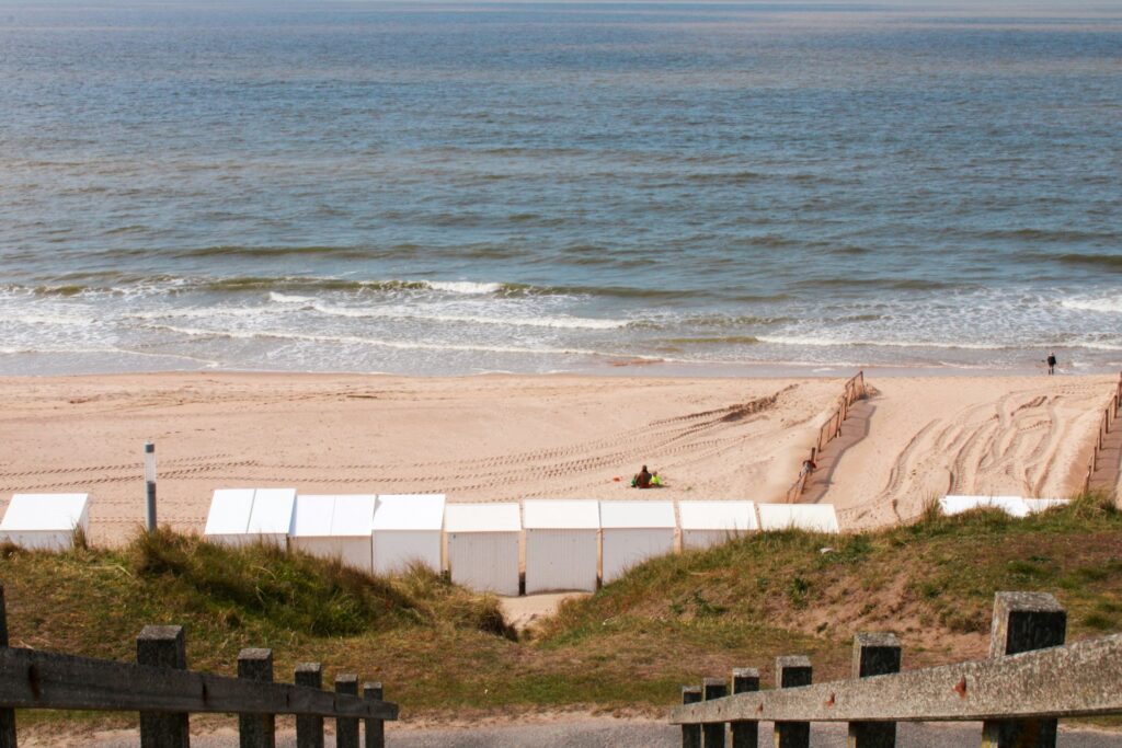 A landscape view of De Haan beach with some easy to ride waves in the water.
